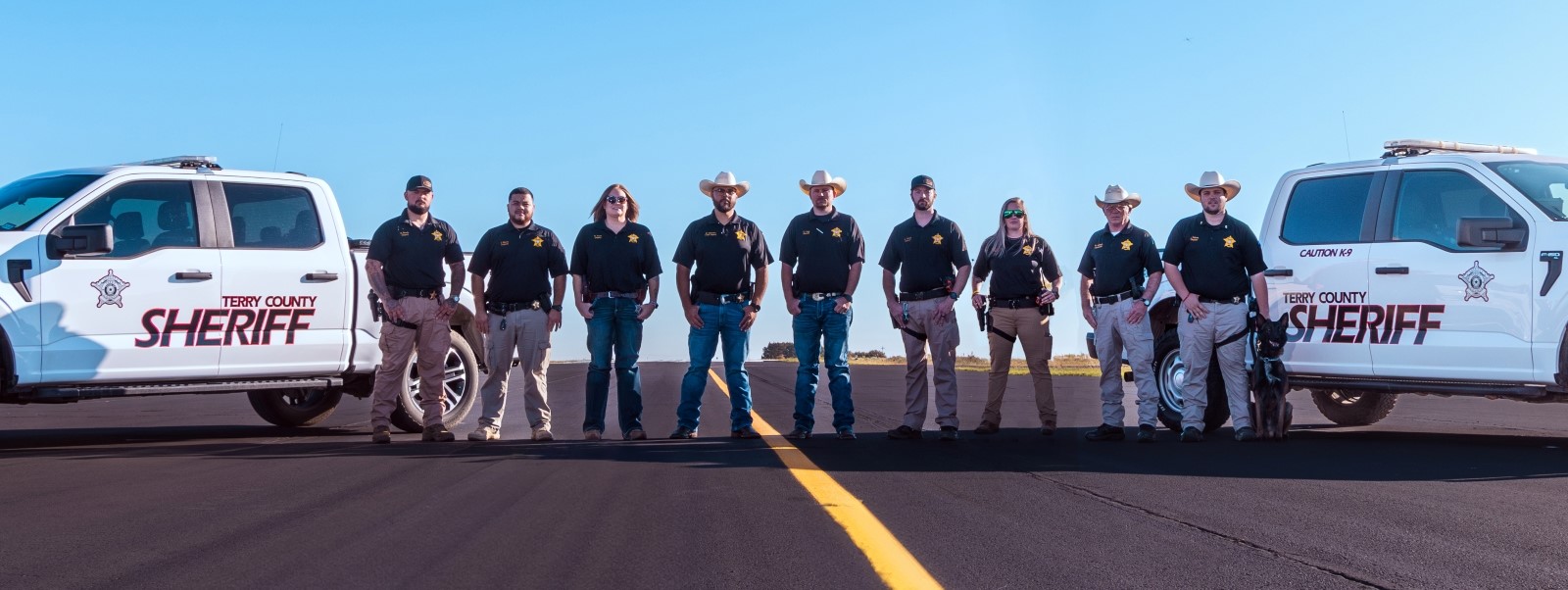 Terry County Sheriff Staff and K9 with two patrol trucks behind them.